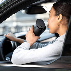 Persona bebiendo café de un termo negro con tapa deslizante en un coche, parte de Take away, Fellow, EspressoGear, todo sobre café.