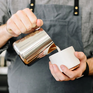 Barista vierte leche desde una jarra pulida de acero inoxidable, parte de Accesorios para Espresso y Jarra para leche, todo sobre café.