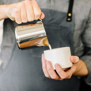 Barista vierte leche desde una jarra pulida de acero inoxidable, parte de Accesorios para Espresso y Jarra para leche, todo sobre café.