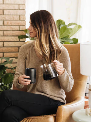 Mujer con suéter beige sosteniendo una jarra de servicio de espresso para barista de vidrio, diseño moderno, Últimas novedades, todo sobre café.