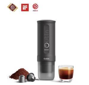 Cafetera espresso portátil en tono gris con cápsulas de café, café molido y espresso en vaso, para uso al aire libre.