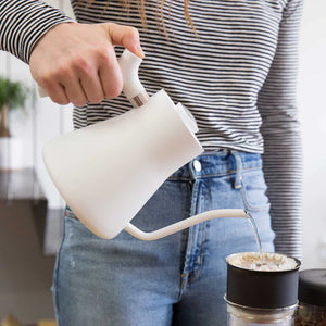 Mano que vierte agua desde una tetera blanca con pico estrecho hacia un filtro de café, parte de EspressoGear, todo sobre café.