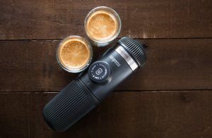 Máquina de espresso portátil con dos tazas de espresso sobre superficie de madera, de cafeteras portátiles y equipo de barista
