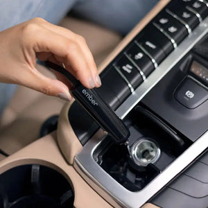 Mano conectando cargador de coche para taza eléctrica Ember en el encendedor del coche para una carga cómoda.